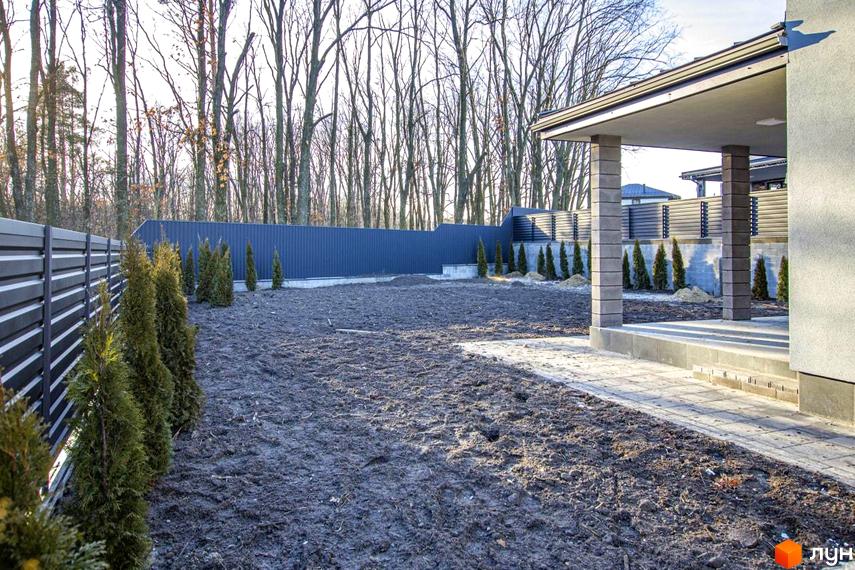 Котеджне містечко КМ NOVYI SVIT: огороджена ділянка з молодими туями та будівельними роботами. На задньому плані паркан та дерева.