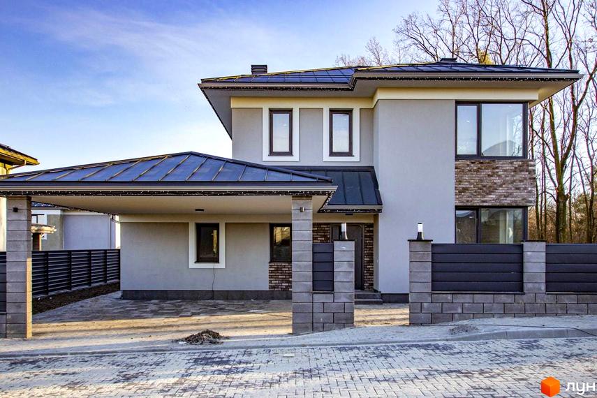 Котеджне містечко КМ NOVYI SVIT: двоповерховий будинок з сірим фасадом, темним дахом та навісом для авто. Прибудинкова територія з бруківкою та парканом.