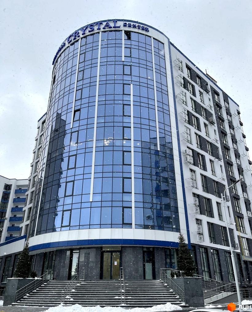 Зовнішній вигляд фасаду новобудови ЖК Crystal Center з панорамним склінням та сходами, що ведуть до входу. Навколо будівлі видно засніжену територію та дерева.