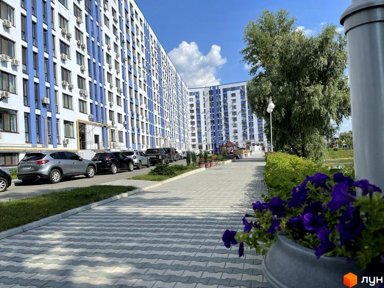 Житловий комплекс Рів'єра з біло-синім фасадом та кондиціонерами, доглянута прибудинкова територія з доріжками та зеленню.