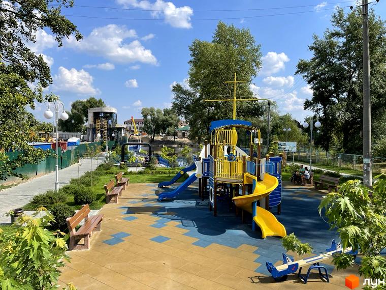 Дитячий майданчик у ЖК Рів'єра з ігровим кораблем та гірками. Поруч розташовані лавки та зелені насадження.