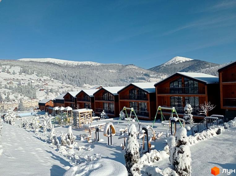 Зимовий краєвид Котеджного містечка Phoenix Relax Park з дерев'яними котеджами та дитячим майданчиком, вкритим снігом.