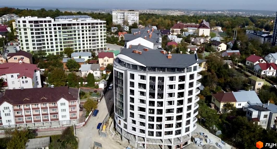 Зображення Житлового комплексу Трускавецька Фортеця. Круглий будинок з великими вікнами та сірим дахом, навколо зелені насадження та інші будівлі.