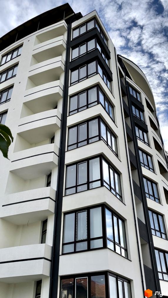 Фасад Житлового комплексу Трускавецька Фортеця: білі стіни, темні віконні рами та кутові вікна. Будівля має балкони з чіткими горизонтальними лініями.