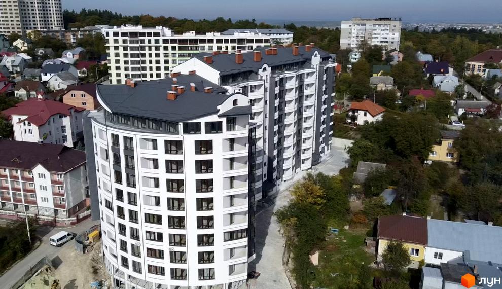 Житловий комплекс Трускавецька Фортеця: вид зверху на багатоповерховий будинок з білими фасадами та темними дахами, оточений приватними будинками та зеленню.