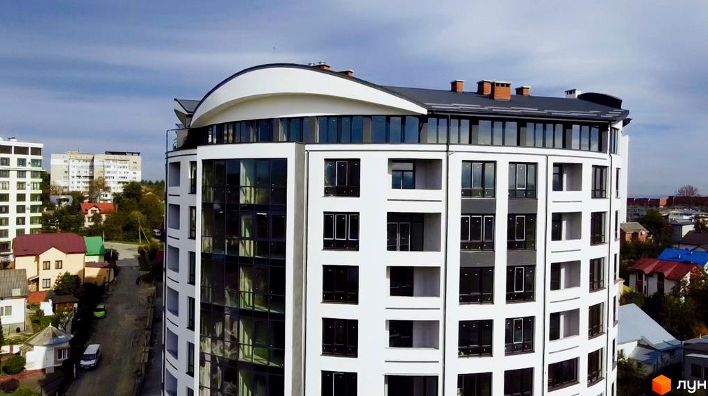 Новобудова Трускавецька Фортеця: біла будівля округлої форми з темними вікнами та вигнутим дахом, розташована серед міської забудови.