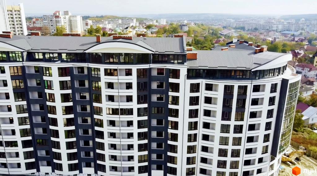 Житловий комплекс Трускавецька Фортеця – багатоповерхова будівля з вигнутим фасадом, білими та темно-сірими панелями. Вид на новобудову серед міської забудови.