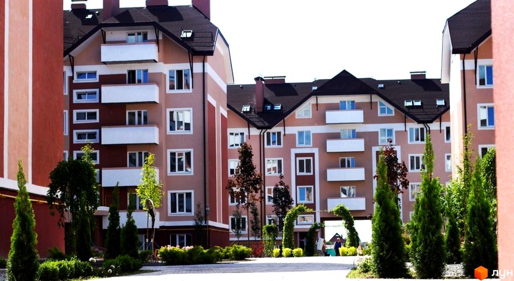 Зовнішній вигляд житлового комплексу Новатор з балконами та прибудинковою територією з зеленими насадженнями.