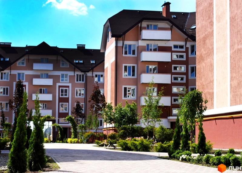 Житловий комплекс Новатор з сучасними фасадами та прибудинковою територією, озелененою деревами та кущами.