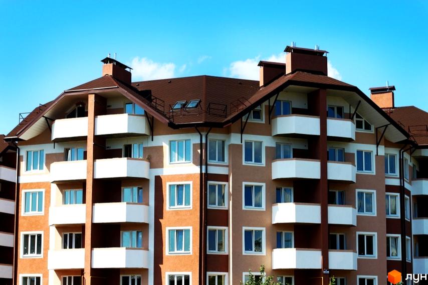 Зовнішній вигляд будинку житлового комплексу Новатор з балконами та вікнами. Прибудинкова територія озеленена та облаштована.