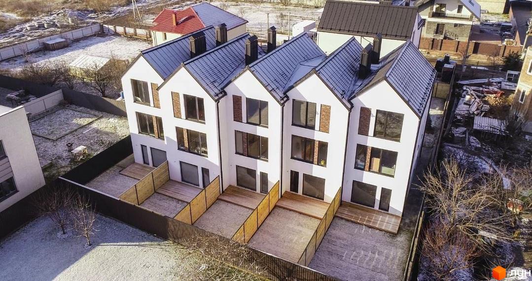 Таунхауси DOMA NOVA з білими фасадами та темними дахами, з індивідуальними дерев'яними терасами та огородженими ділянками.