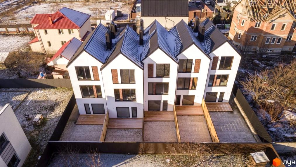 Зовнішній вигляд таунхаусів DOMA NOVA з білими фасадами та темними дахами, розташованих на засніженій ділянці з дерев'яними терасами.