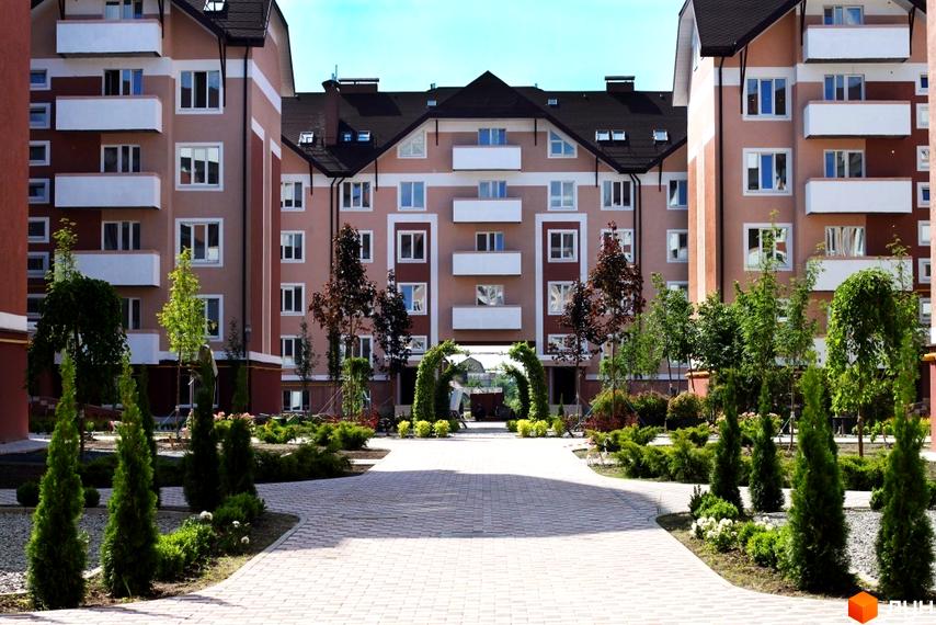 Житловий комплекс Новатор з фасадом у світлих тонах та прибудинковою територією з зеленими насадженнями і доріжками.