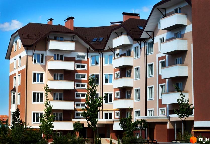 Зовнішній вигляд житлового комплексу Новатор з балконами та вікнами. Прибудинкова територія озеленена деревами та кущами.