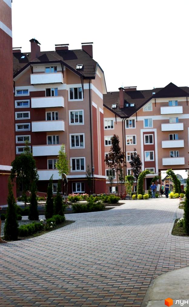 Житловий комплекс Новатор з фасадами світло-бежевого та коричневого кольорів, балконами та доглянутою прибудинковою територією з арками та зеленими насадженнями.