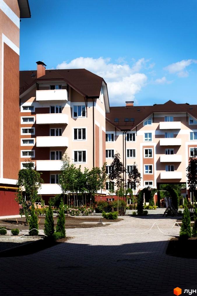 Житловий комплекс Новатор: фасади будівель з балконами та вікнами, прибудинкова територія з деревами та бруківкою.