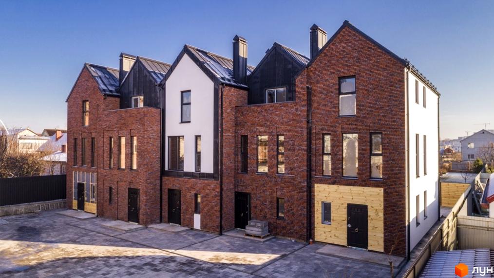 Таунхауси DOMA NOVA. Цегляні та білі фасади з чорним металевим дахом, вікна з чорними рамами, перед будинками вимощена сіра бруківка.