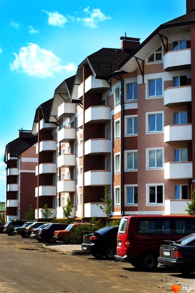 Зовнішній вигляд житлового комплексу ЖК Новатор з балконами та вікнами, парковка автомобілів перед будинком.