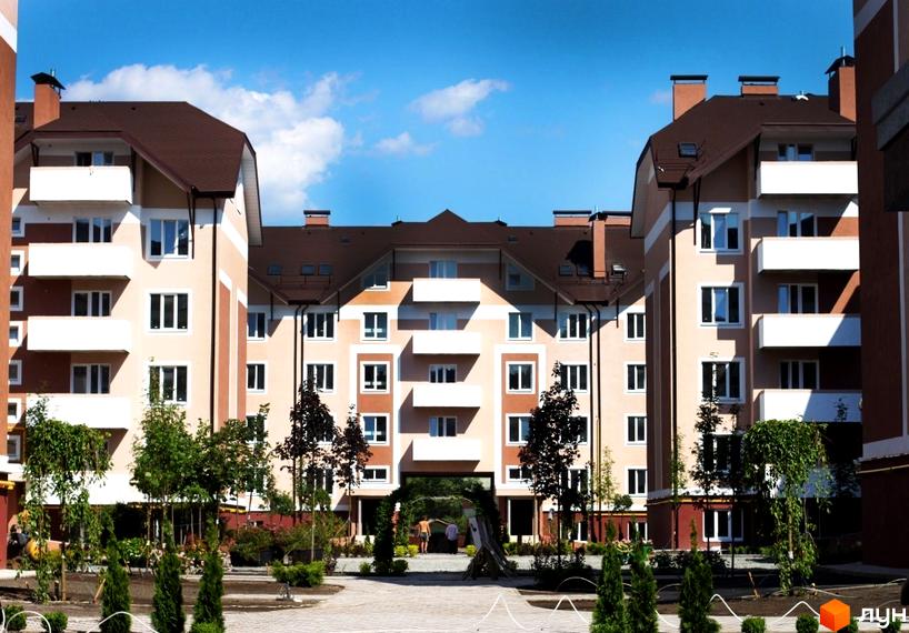 Житловий комплекс Новатор з фасадами світло-бежевого кольору та коричневими дахами. Прибудинкова територія з зеленими насадженнями та доріжками.