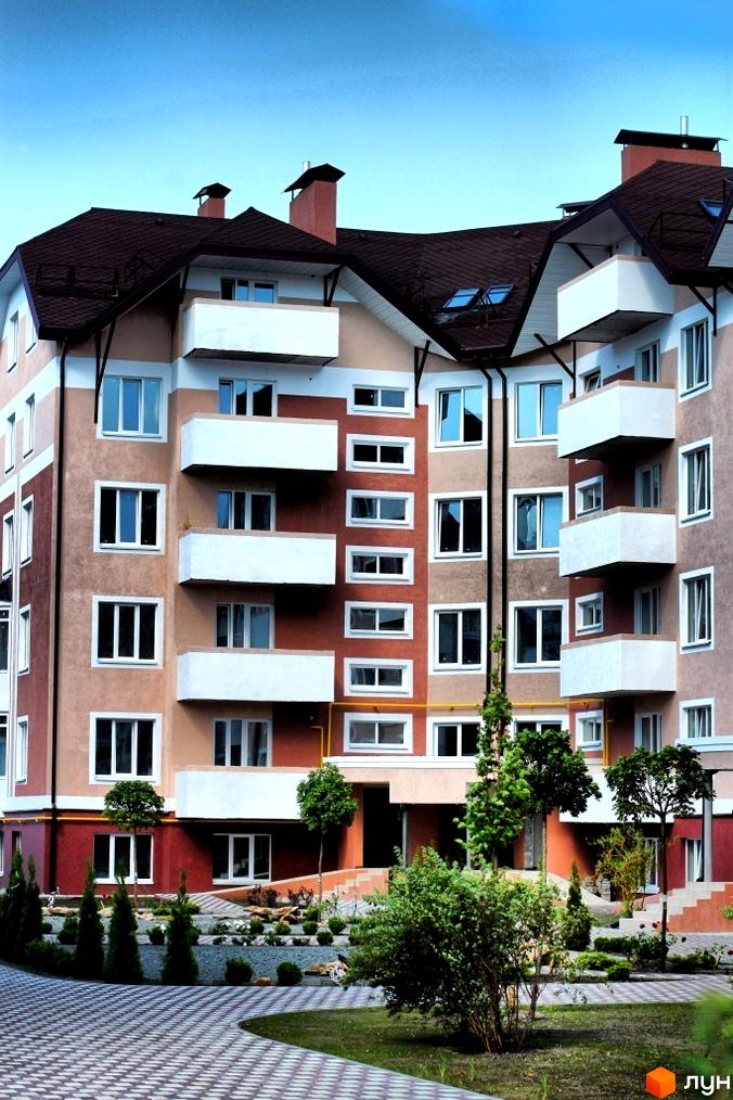 Зовнішній вигляд будинку житлового комплексу Новатор з балконами та вікнами. Прибудинкова територія з доріжками та зеленими насадженнями.