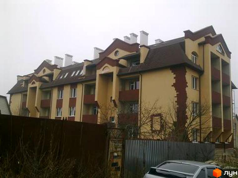 Зовнішній вигляд житлового комплексу на вул. Першотравнева, 11 з балконами та дахом. Прибудинкова територія з зеленими насадженнями.