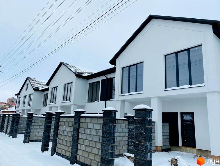 Новобудова на вул. Мельника, 25, з білими фасадами та темними вікнами, огороджена парканом з цегли та каменю, взимку.