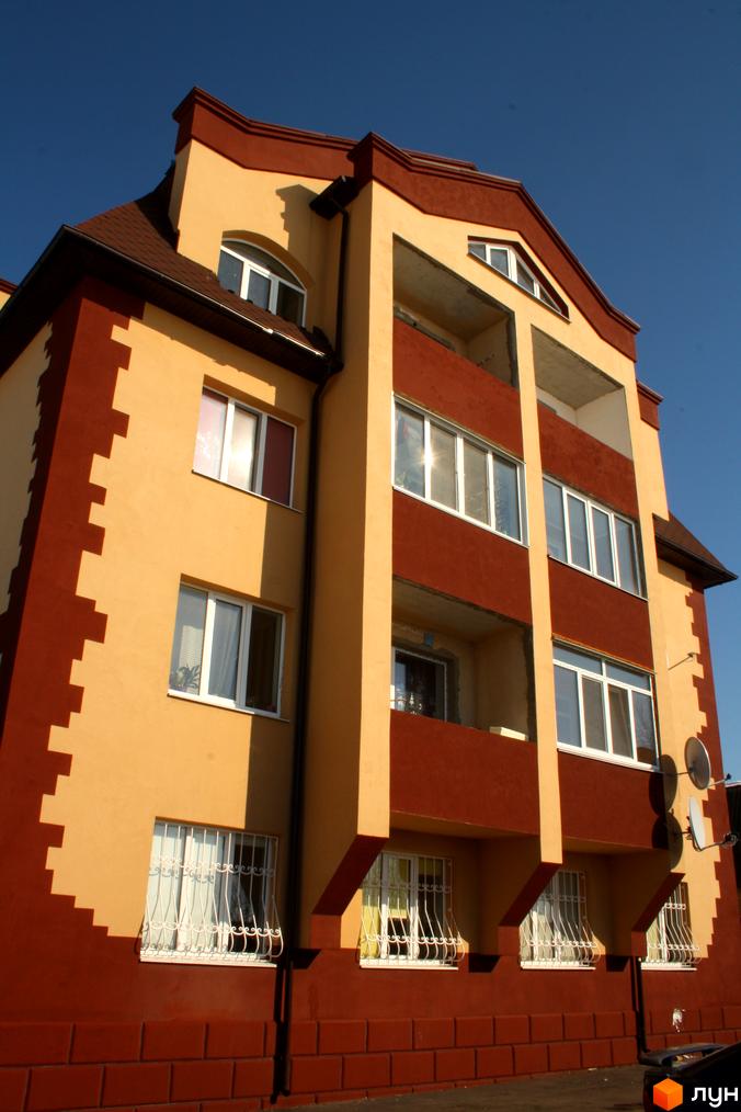 Житловий комплекс на вул. Першотравнева, 11, з фасадом жовтого та червоного кольорів. Прибудинкова територія з вікнами та балконами.