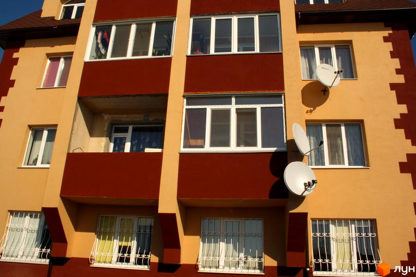 Фасад будинку на вул. Першотравнева, 11 з вікнами та балконами. Прибудинкова територія з елементами благоустрою.