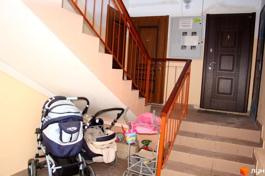Вхідна зона житлового комплексу з сходами та дитячими візками. Сучасні двері та освітлення в коридорі.