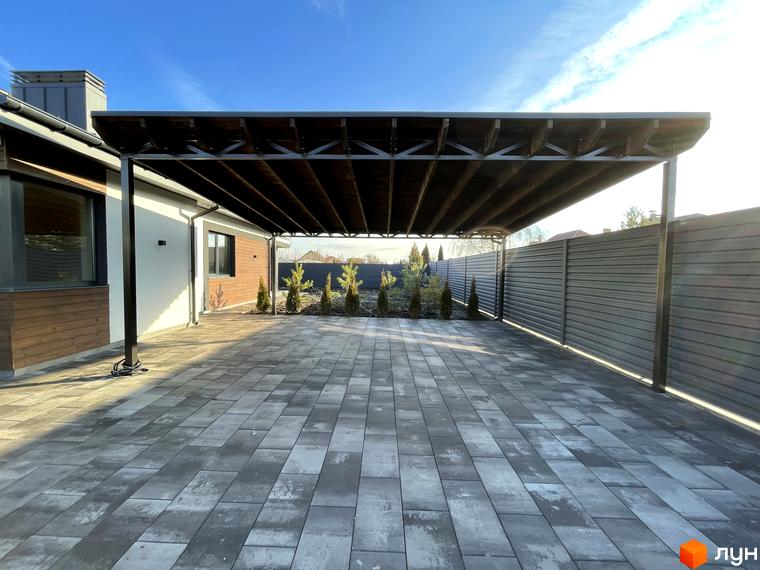 Сучасний навіс для автомобілів біля будинку з дерев'яною обшивкою та бруківкою на вулиці Мазепи. Територія комплексу доглянута з молодими туями.