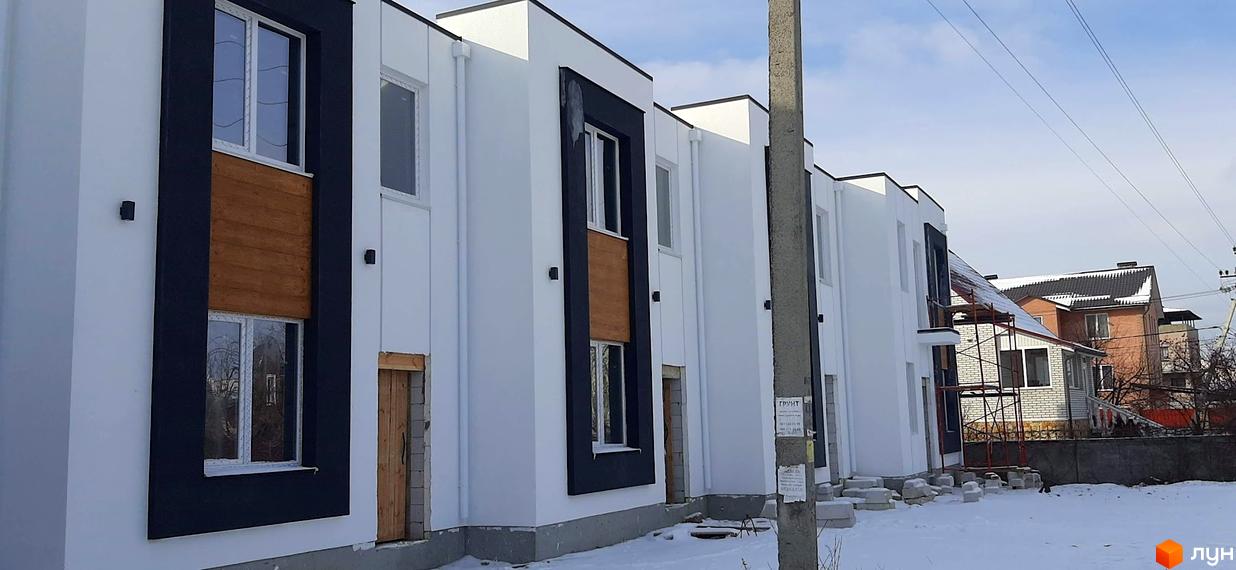 Котеджне містечко Holland Park. Фасади будинків білі з чорними елементами та дерев'яними вставками, навколо сніг.