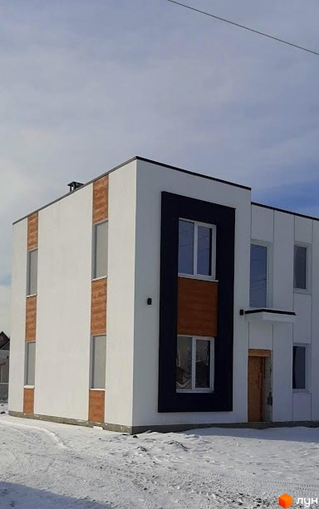 Білий двоповерховий будинок Котеджного містечка Holland Park з темними та коричневими акцентами на фасаді, розташований на засніженій ділянці.