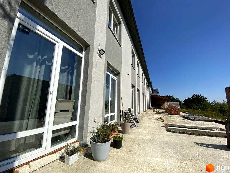 Зовнішній вигляд таунхаусів Hodillywood 1.0 з великими вікнами та сірим фасадом. На прибудинковій території видно будівельні матеріали та зелень.