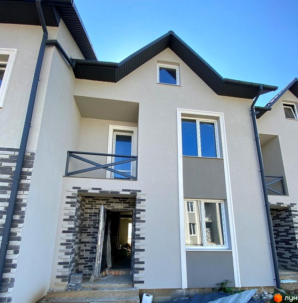 Зовнішній вигляд таунхаусів Hodillywood 2.0 з сірим фасадом та цегляним оздобленням цоколя. Навколо будинку видно будівельні матеріали та елементи фасаду.