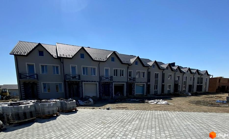 Таунхауси Hodillywood 2.0 – це ряд сірих двоповерхових будинків з темними дахами та балконами. Перед будинками розташована вимощена сіра плитка та будівельні матеріали.