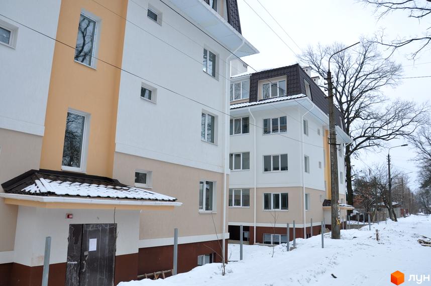 Зовнішній вигляд будинку житлового комплексу ЖК Ворзель з білими та кремовими стінами. Прибудинкова територія в снігу з деревами та електричними стовпами.