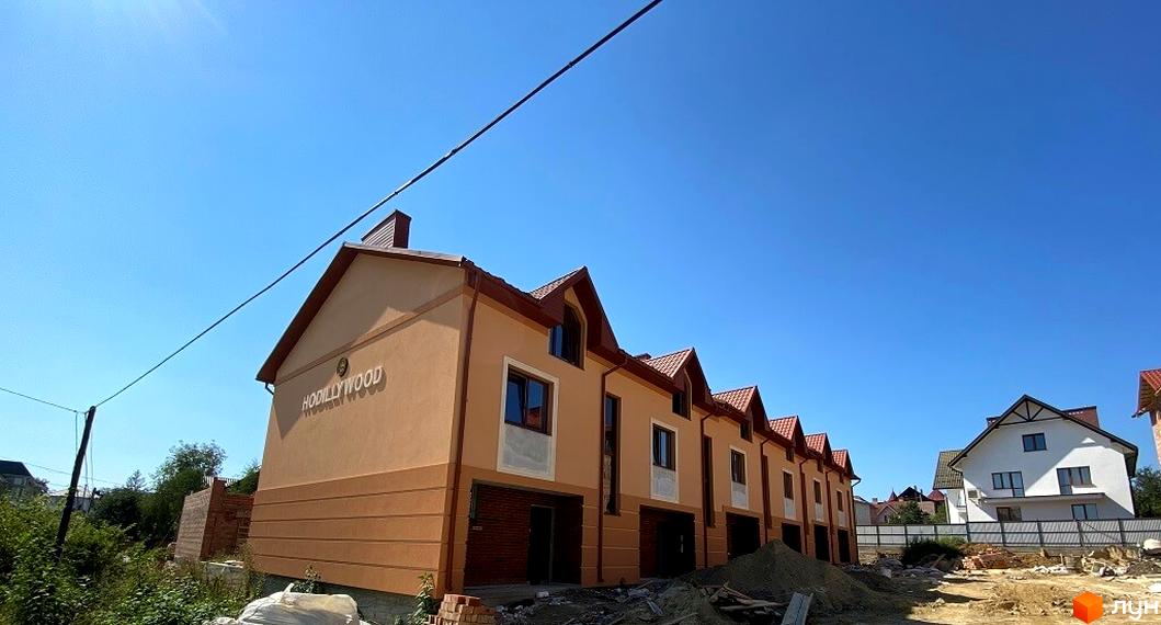 Таунхауси Hodillywood 4.0 з коричневими дахами та світло-бежевими фасадами. Навколо новобудови видно будівельні матеріали та зелені насадження.