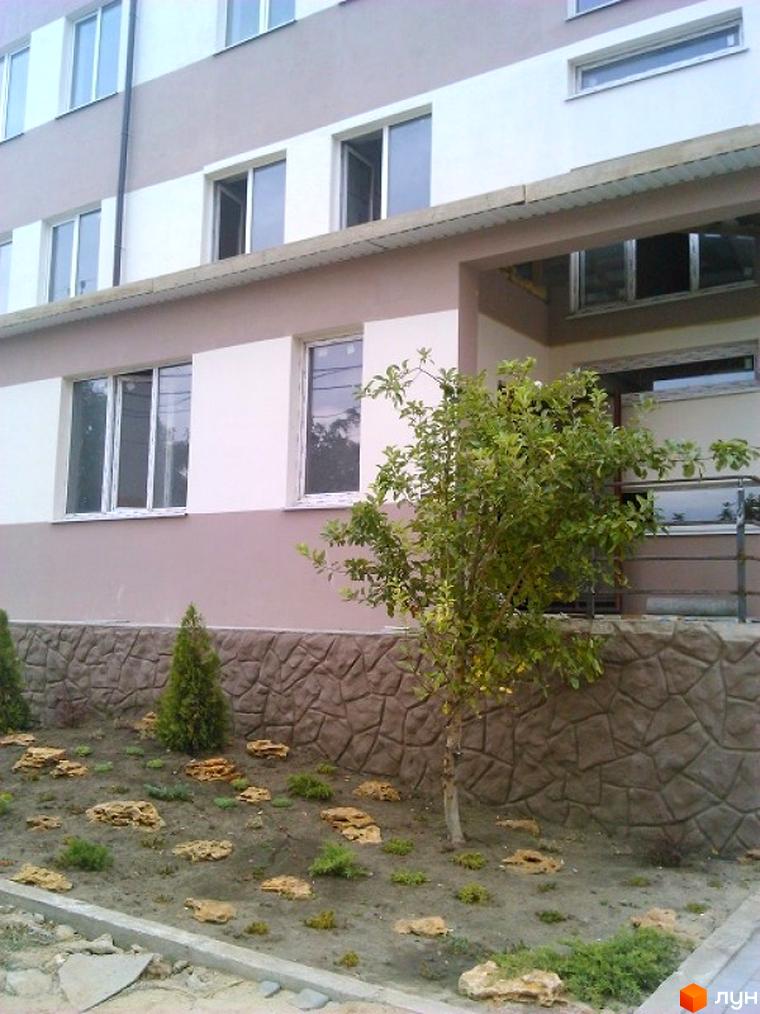 Житловий комплекс Софіївський дом: фасад з білими та світло-коричневими смугами, вікна. Прибудинкова територія з кам'яною стіною, деревами та камінням.