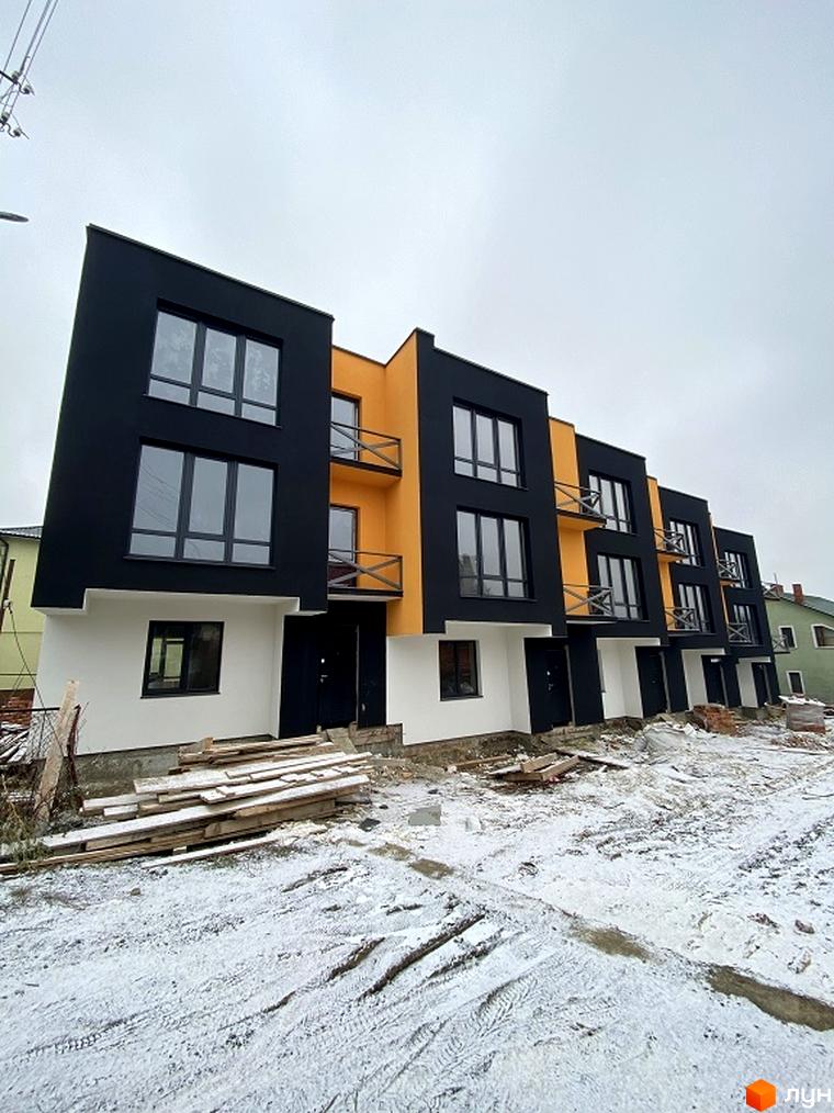 Зовнішній вигляд таунхаусів Hodillywood 6.0 з чорним та жовтим фасадом, вікнами та балконами. На передньому плані видно ділянку з дерев'яними дошками та снігом.