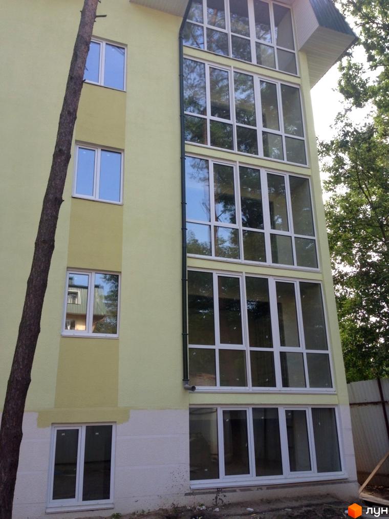 Зовнішній вигляд будинку ЖК Теплий дім з великими вікнами та жовтою фасадною фарбою. Прибудинкова територія з зеленими насадженнями.