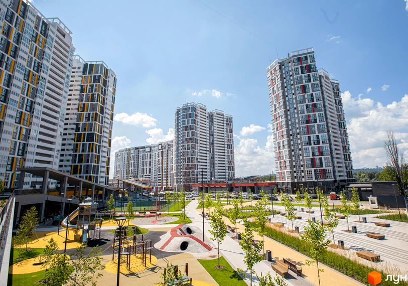 Високі будинки житлового комплексу Русанівська Гавань з яскравими фасадами. На території комплексу дитячий майданчик та зелені зони.