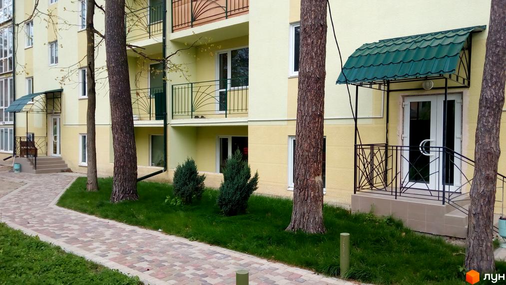 Житловий комплекс Теплий дім з жовтим фасадом та зеленими балконами. Приблизно біля будинку розташована доглянута територія з газоном і доріжками.