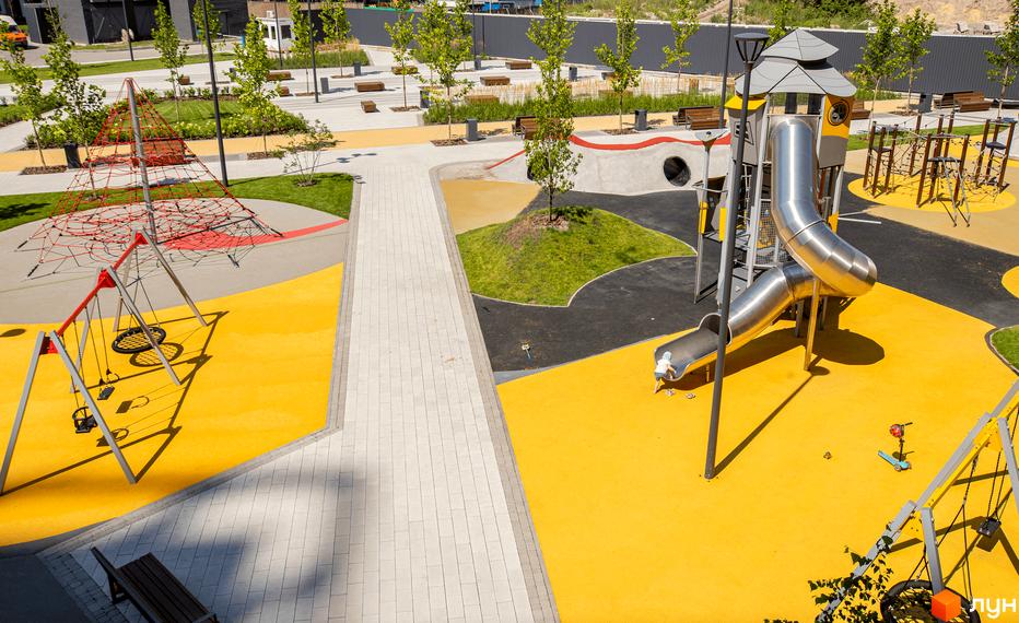 Дитячий майданчик у житловому комплексі. Яскравий жовтий колір покриття, гірка, гойдалки та сітчастий лабіринт для розваг дітей.