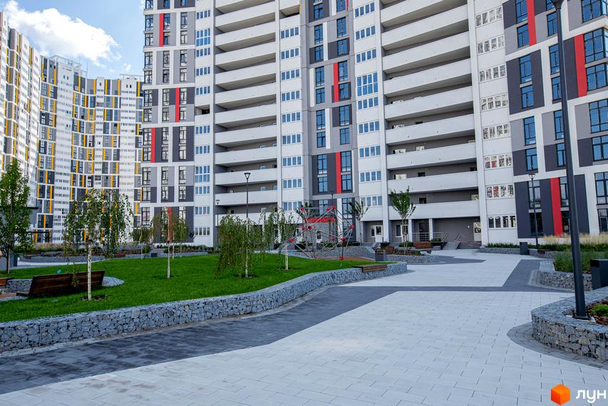 Русанівська Гавань: будинки з сірими, білими, жовтими та червоними фасадами. Прибудинкова територія має газони, дерева, дитячий майданчик та доріжки.