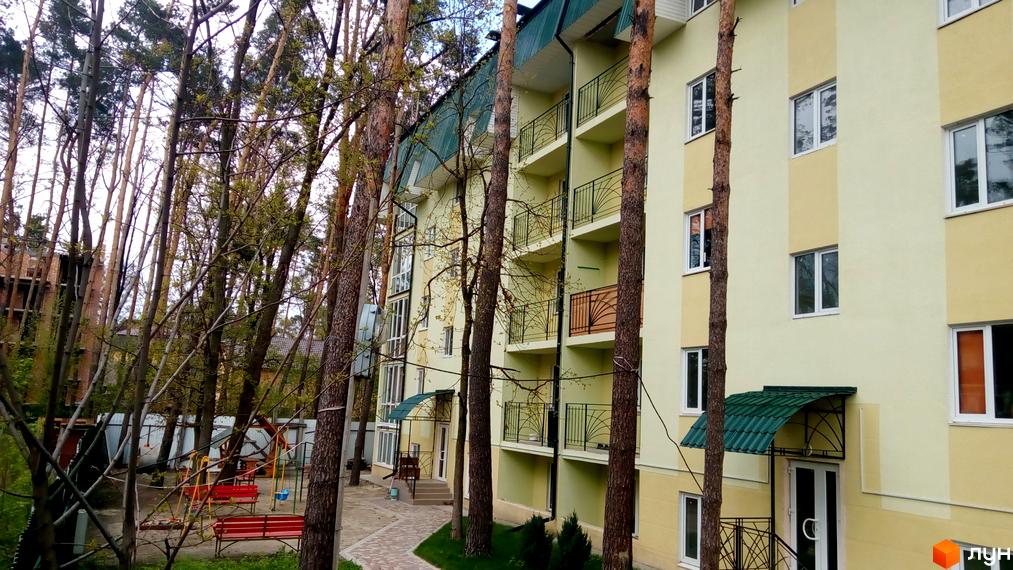Зовнішній вигляд житлового комплексу Теплий дім з зеленими балконами та прибудинковою територією з дитячим майданчиком.