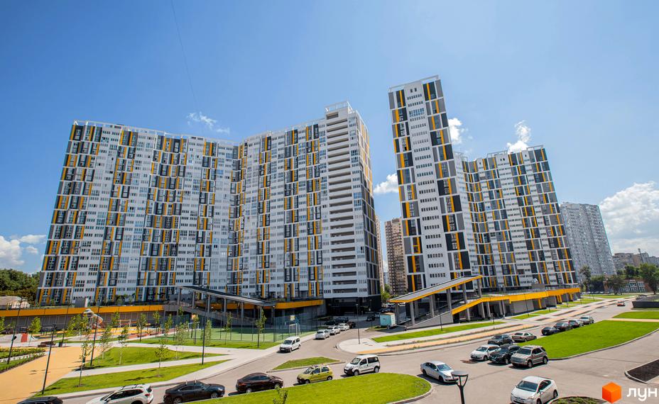 Житловий комплекс Русанівська Гавань з висотними будинками з білими фасадами та жовтими вставками. На території комплексу є зелені зони, парковка та дорога з автомобілями.