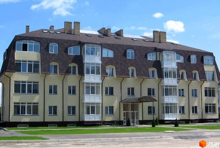 Житловий комплекс Чубинське має світлий фасад та темно-коричневий дах з мансардними вікнами. Перед будинком розташований зелений газон та асфальтована доріжка.
