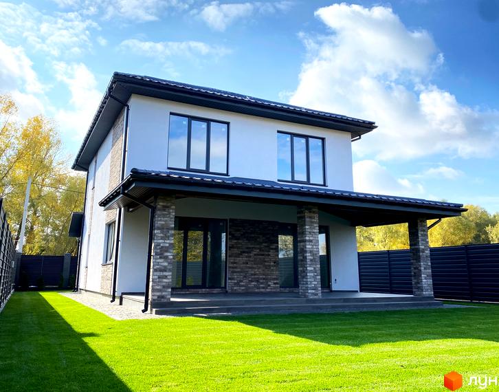Котеджне містечко Щастя: двоповерховий будинок з білим фасадом, темним дахом та кам'яними елементами. Перед будинком зелений газон.