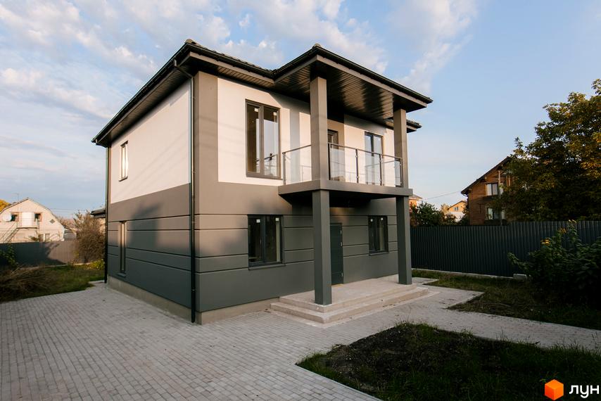 Двоповерховий будинок з балконом, оздоблений у сірих тонах. Перед будинком викладена бруківка, є невеликий газон.