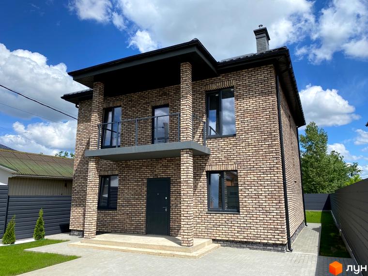 Двоповерховий будинок з цегляною кладкою, балконом та темними вікнами. На прибудинковій території газон та доріжка з плиткою.